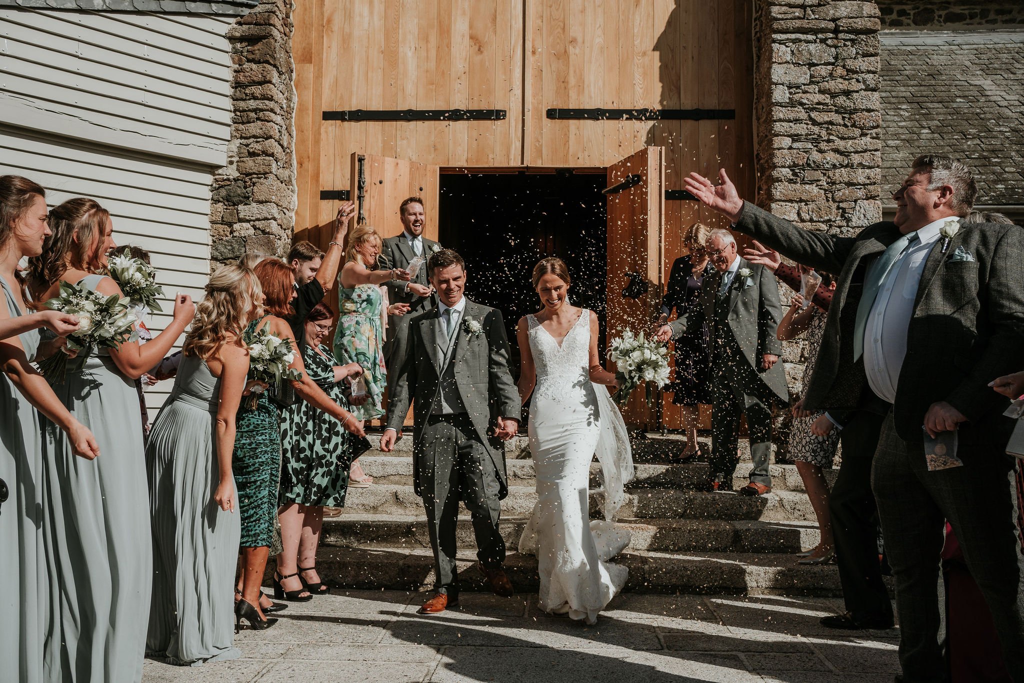 Exterior shot of bride and groom confetti after ceremony at The Great Barn Devon luxury 15th century wedding venue near Exeter UK