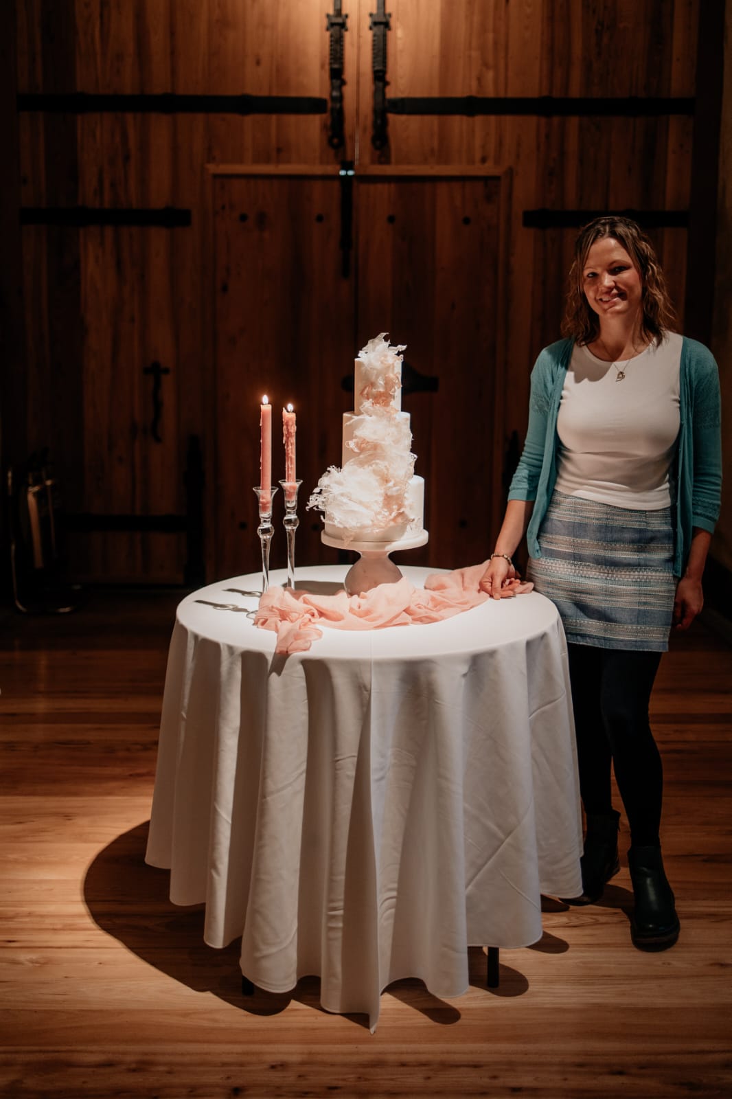 Nicole of Sweet Satisfaction Cake Design stood next to a Wedding cake table on display inside The Great Barn Devon, luxury 15th century wedding venue in the countryside near Exeter Devon UK