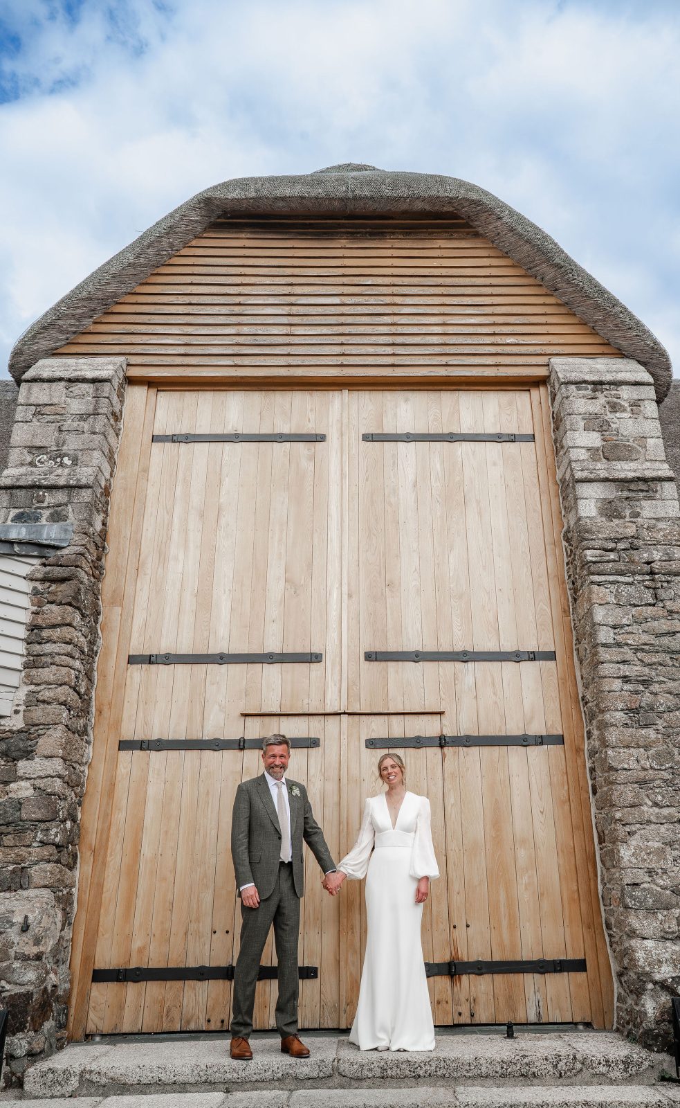 Sarah & Tom standing outside the doors of The great Barn Devon on their wedding day | Barn Wedding Venue in Devon