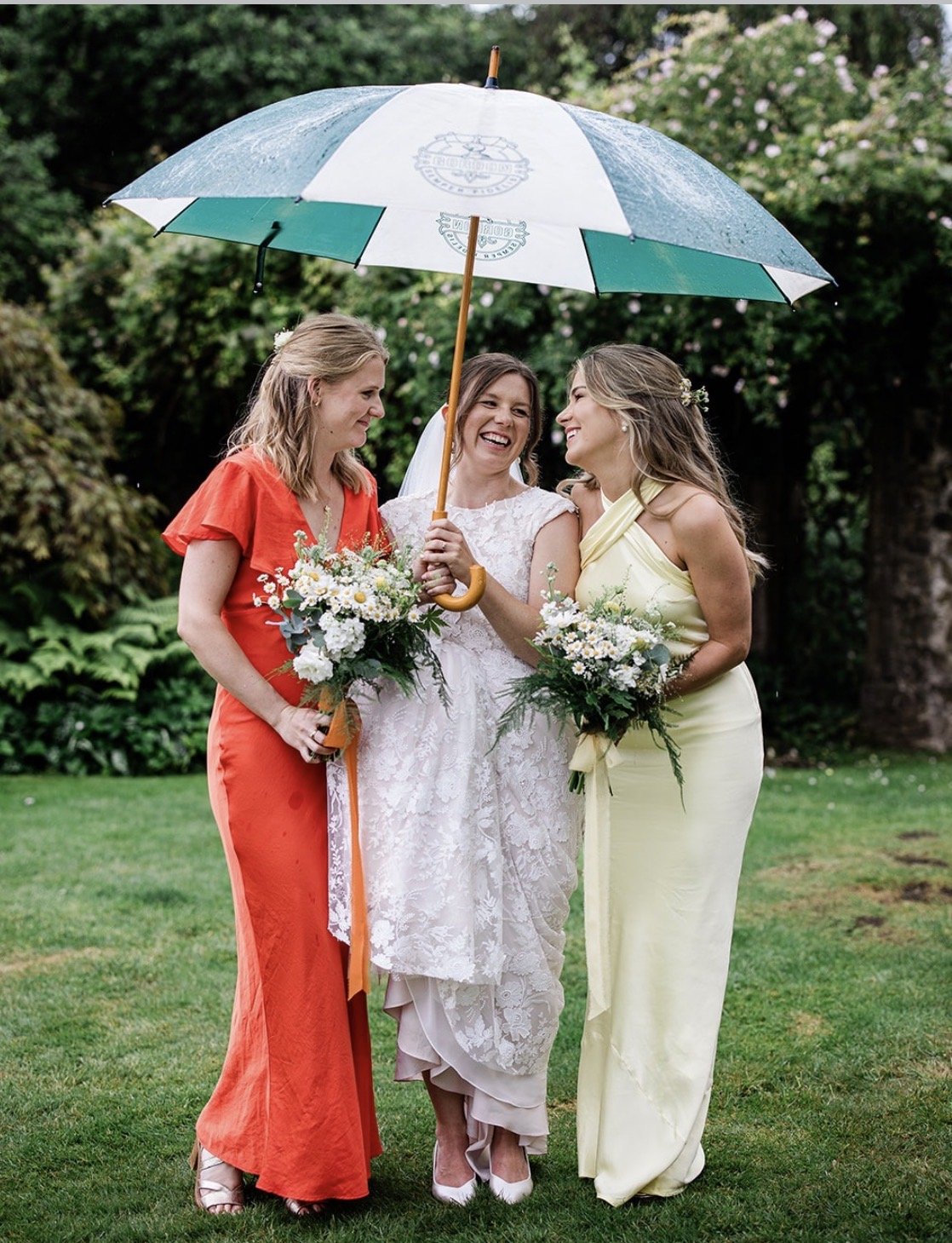bride and bridesmaids stood under an umbrella in the gardens of the great barn devon