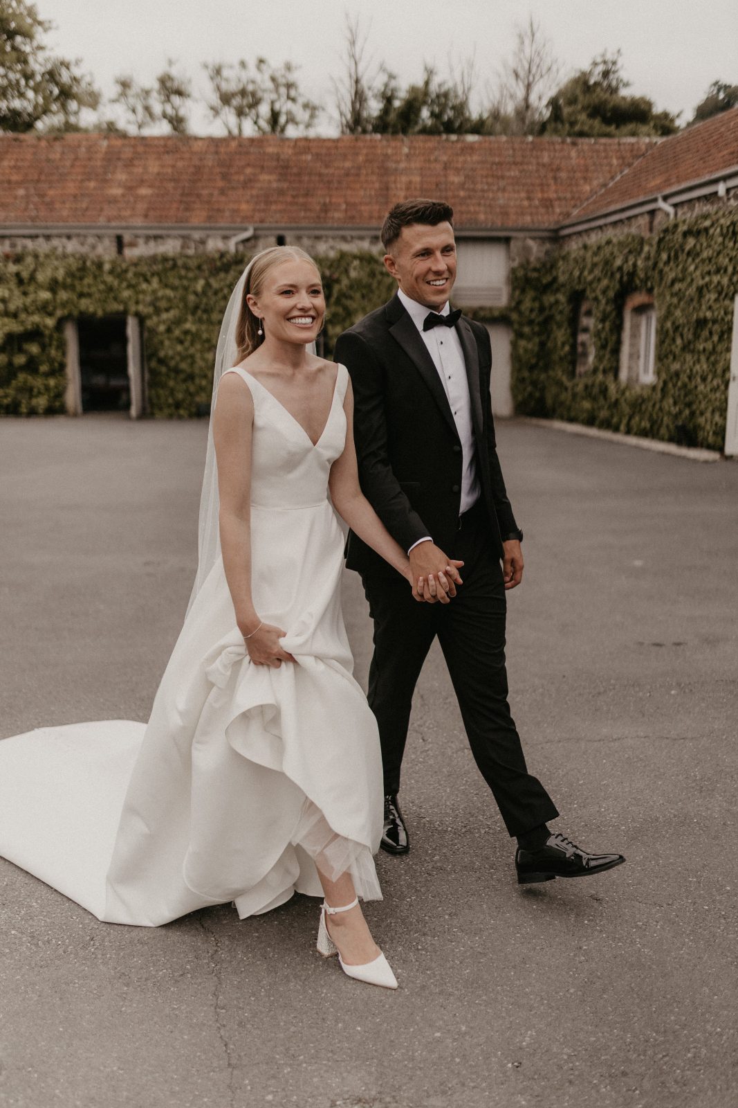 bride and groom walking hand in hand through courtyard at wedding venue in devon